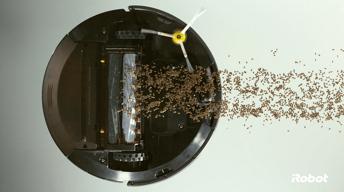 A bottom view of Roomba showing side brushes and 2 extractor bars while vacuuming pieces of dirt.